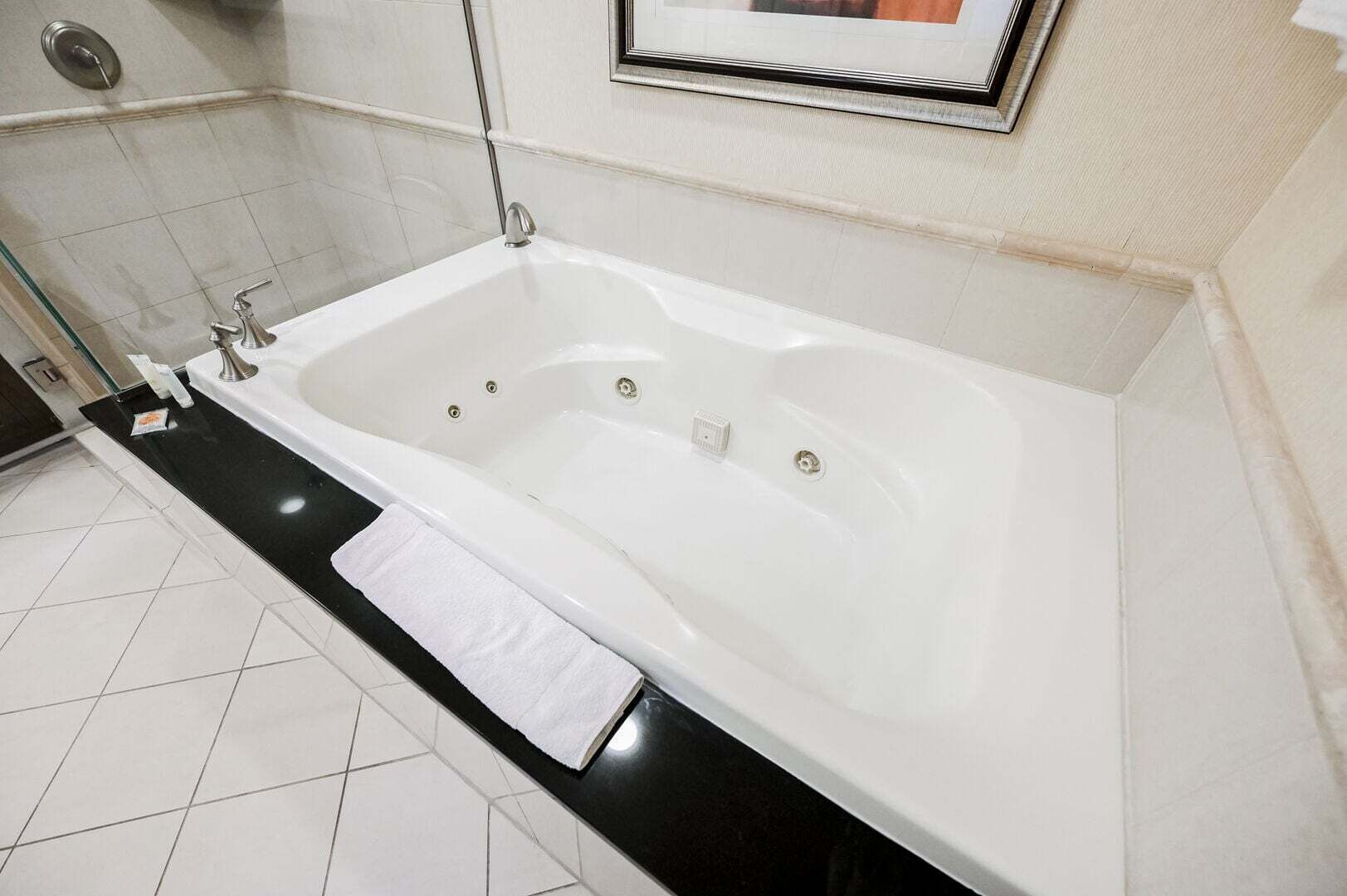 Une salle de bain moderne avec une baignoire blanche, un plan de toilette noir et un sol carrelé.