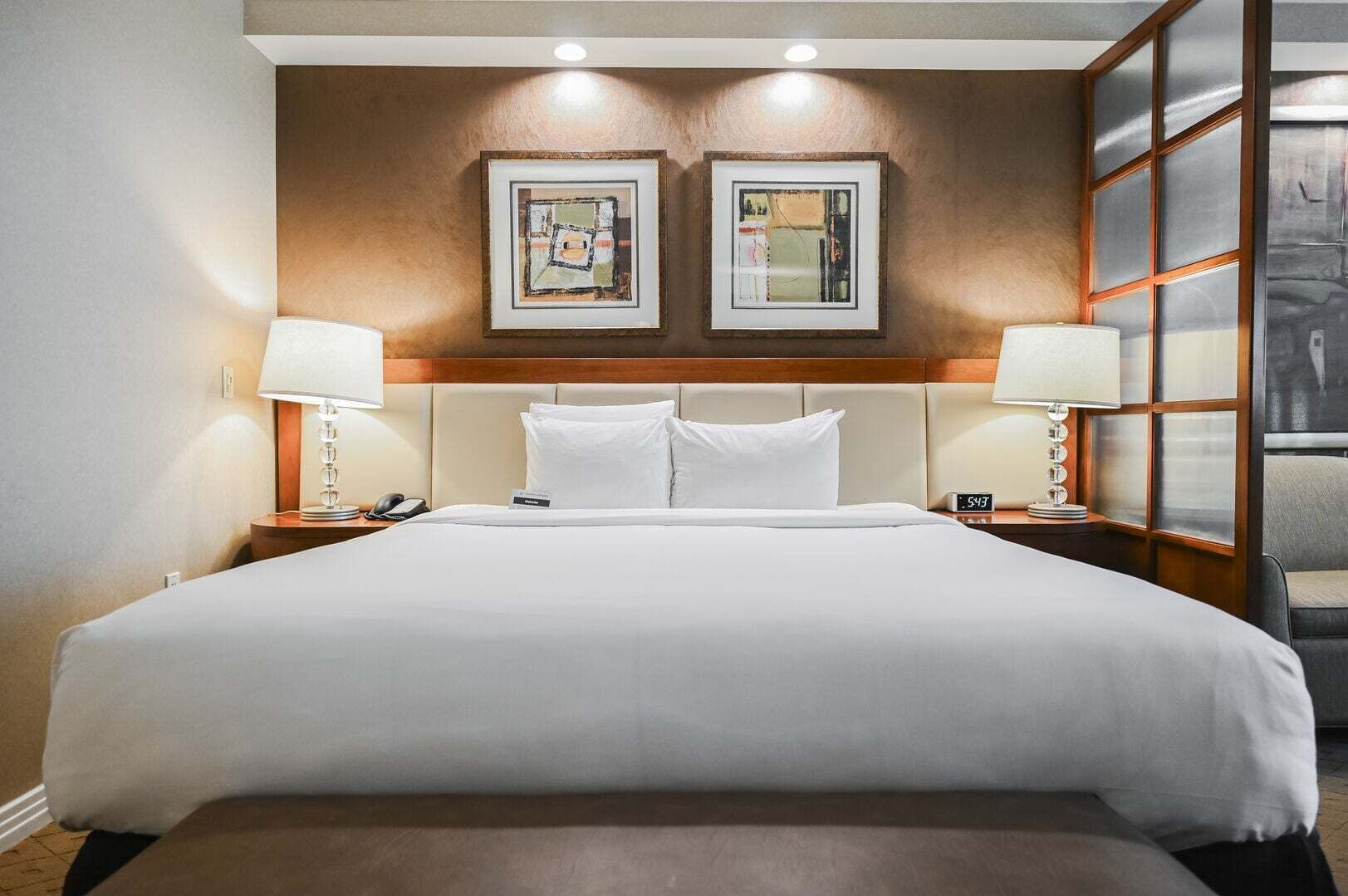 Una habitación de hotel con una cama grande, dos mesitas de noche con lámparas, un reloj y dos cuadros en la pared.