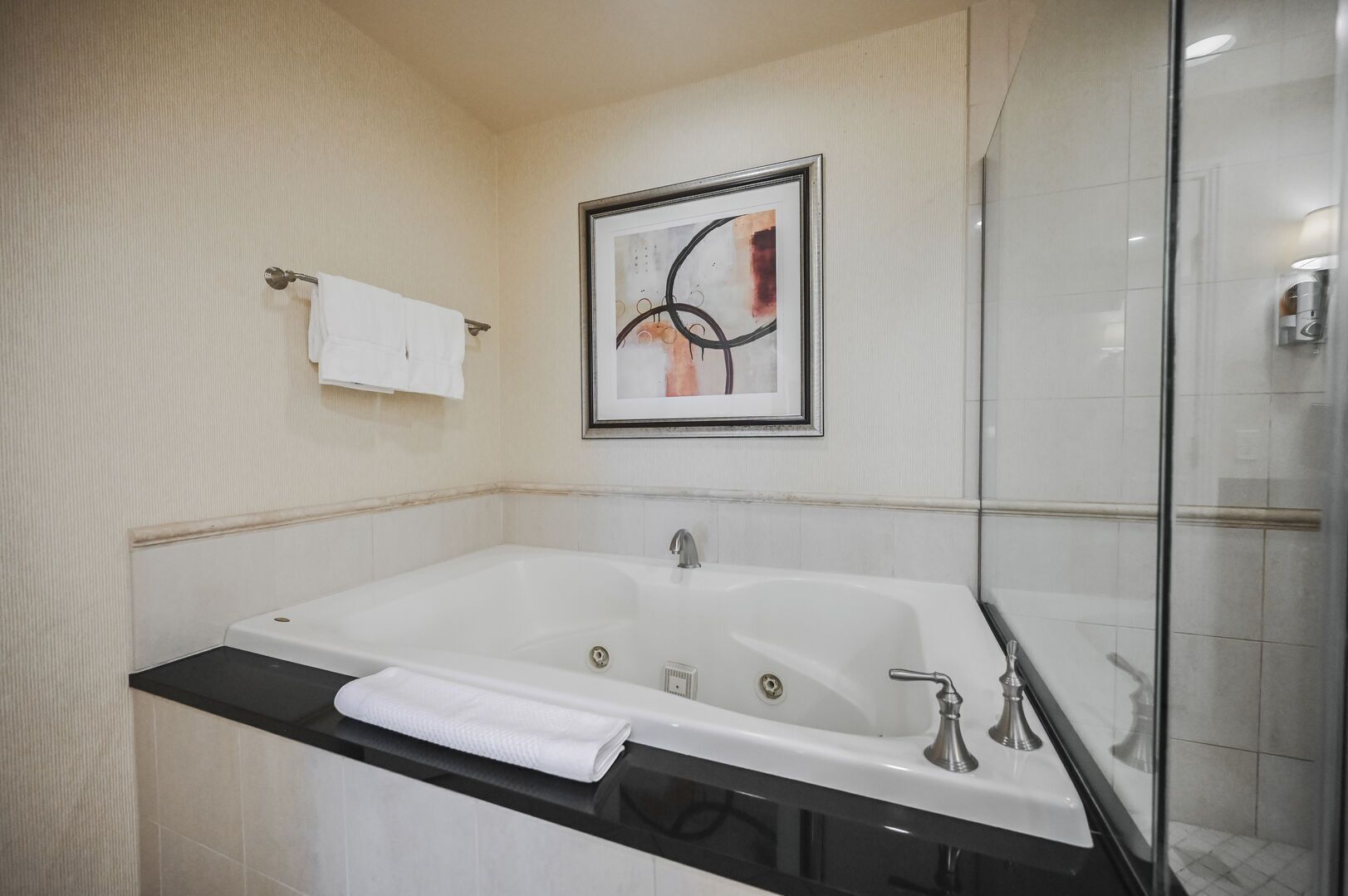 Ein modernes Badezimmer mit einer großen Badewanne, einer Duschkabine aus Glas und einem gerahmten abstrakten Kunstwerk an der Wand.