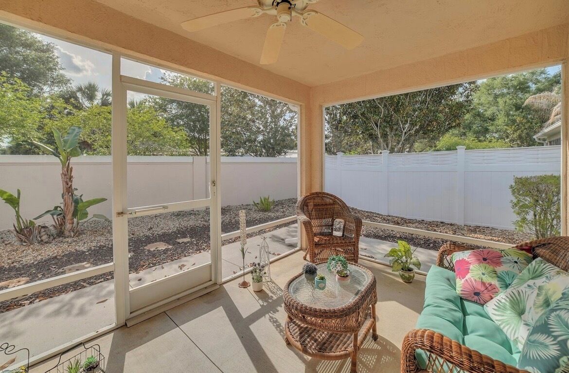 A covered patio with wicker furniture, a glass table, and potted plants.