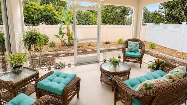 A sunlit patio area with wicker furniture, a ceiling fan, and a view of a garden through glass doors.
