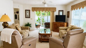 A living room with two leather sofas, a glass coffee table, a television, and a ceiling fan.