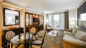 Een hotelkamer met een zithoek, een bank, een televisie en een groot raam met gordijnen.