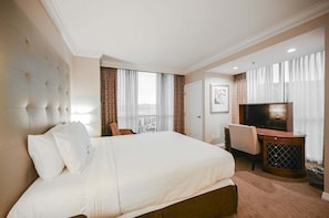 Ein Hotelzimmer mit einem großen Bett, einem Fernseher, einem Schreibtisch und einem Sessel.