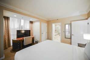 Een hotelkamer met een groot bed, een televisietoestel, een bureau met stoel, een spiegel en een badkamer die zichtbaar is door een open deur.