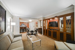 A living room with a sofa, a glass coffee table, a dining table with chairs, a kitchen area, and a TV in a wooden cabinet. - SVS: One Bedroom | Balcony | Signature at MGM (Las Vegas)