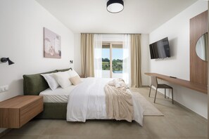 Ein modernes Schlafzimmer mit Bett, Schreibtisch, Fernseher und Blick ins Freie.