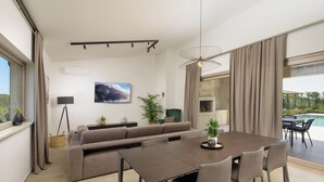 Ett modernt vardagsrum med en soffa, ett matbord, stolar, en tv och utsikt över en pool.