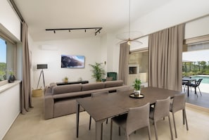 Ein modernes Wohnzimmer mit Sofa, Esstisch, Stühlen, einem Fernseher und Blick auf einen Pool.