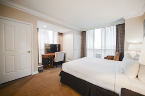 Ein Hotelzimmer mit einem großen Bett, einem Schreibtisch mit Fernseher und Blick auf die Stadt durch die Fenster.