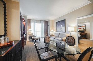 A hotel room with a dining area, a sofa, a TV, and a large window.