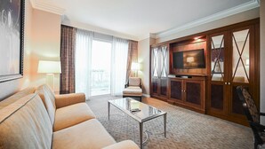 Ett hotellrum med vardagsrumsdel, bestående av en soffa, fåtölj, ett soffbord i glas, en tv och träskåp.