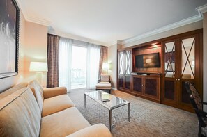 Ein Hotelzimmer mit einer Couch, einem Sessel, einem Glastisch, einem Fernseher und Holzschränken.