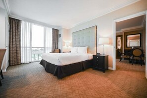 Ein Hotelzimmer mit einem großen Bett, einem Nachttisch, einem Sessel und Blick ins Freie durch ein großes Fenster.