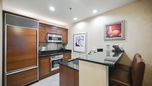 Una cucina moderna con mobili in legno, elettrodomestici in acciaio inossidabile, un'isola in vetro e un angolo salotto con una sedia.