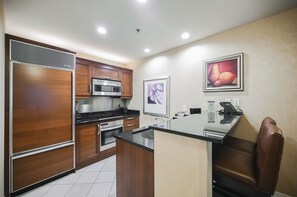 A modern kitchen with wooden cabinets, stainless steel appliances, a glass island, and a seating area with a chair. - SVS: One Bedroom | Strip View Balcony | MGM Signature (Las Vegas)