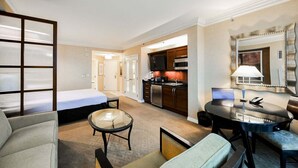 Quarto de hotel com cama, área de estar com mesa e cadeiras, cozinha compacta e banheiro.