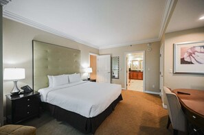 Ein Hotelzimmer mit einem großen Bett, Nachttischen, einem Schreibtisch, einem Sessel und einem durchgehenden Türspalte sichtbaren Badezimmer.