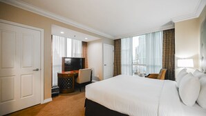 A hotel room with a large bed, a desk with a television, and a view of buildings through the window. - SVS: One Bedroom | Strip View Balcony | MGM Signature (Las Vegas)