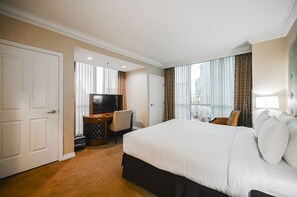 Ein Hotelzimmer mit einem großen Bett, einem Schreibtisch mit Fernseher und Blick auf Gebäude durch das Fenster.