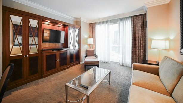 Ein Hotelzimmer mit einer Couch, einem Fernseher, einem Glastisch und einer Sitzecke mit einer Lampe.