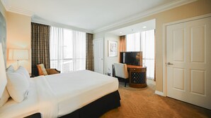 Ein Hotelzimmer mit einem großen Bett, einem Schreibtisch mit Fernseher, einem Sessel und einer Tür.
