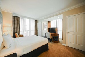 A hotel room with a large bed, a desk with a television, and a door leading to another room. - SVS: One Bedroom | Sphere Strip View Balcony | MGM Signature (Las Vegas)