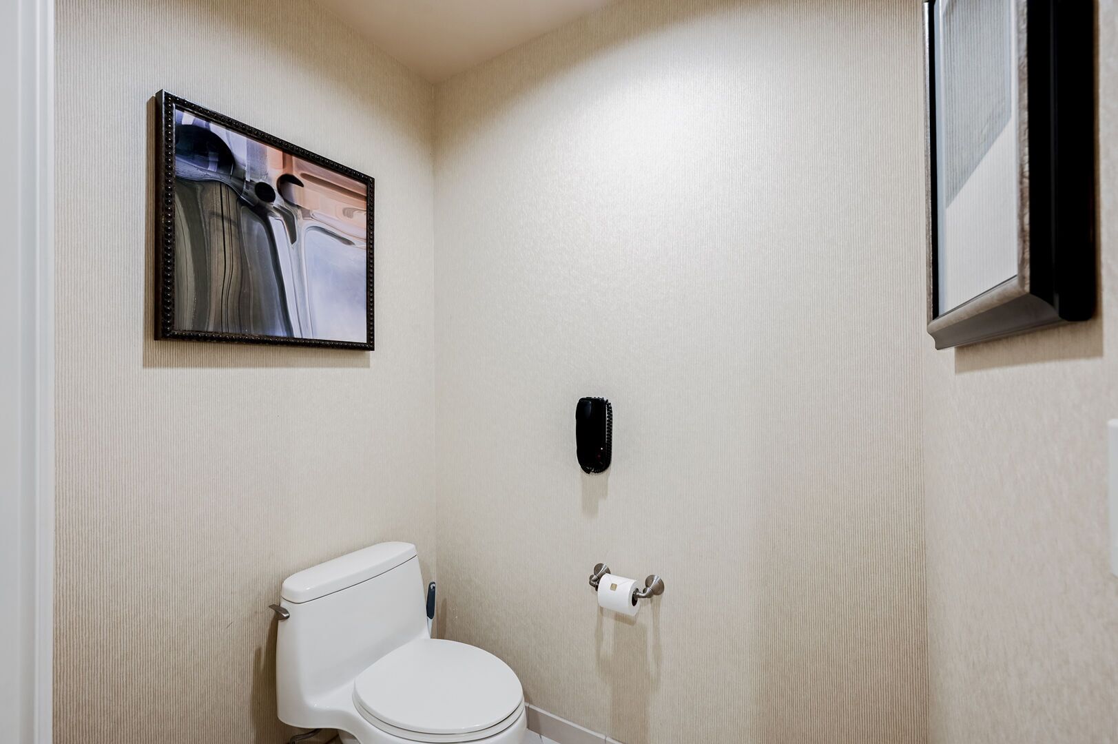 A small bathroom with a toilet, a wall-mounted toilet paper holder, and a framed picture on the wall.