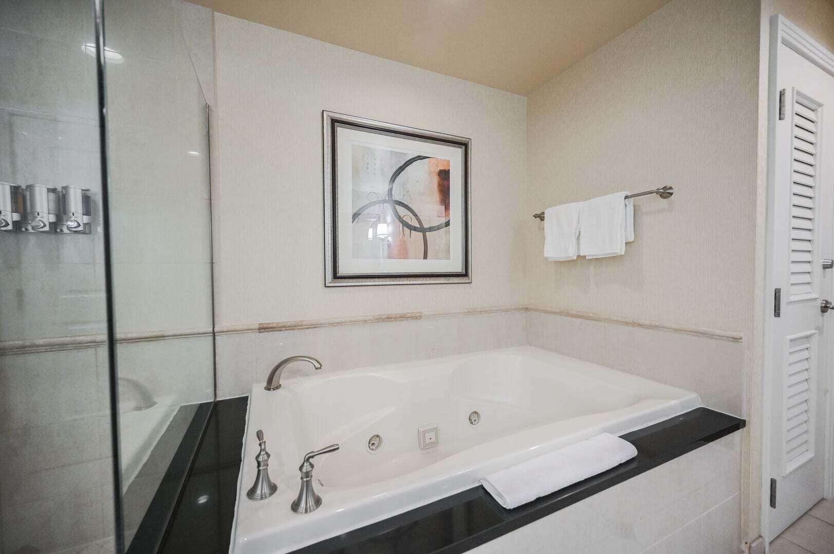 Ett badrum med ett stort badkar, en duschkabin med glasväggar och ett inramat konstverk på väggen.