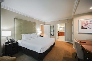 Ein Hotelzimmer mit einem großen Bett, Nachttischen, einem Schreibtisch, einem Sessel und einem durchgehenden Türspalte sichtbaren Badezimmer.