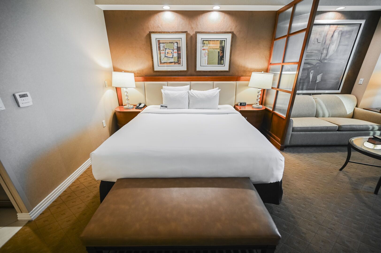 Ein Hotelzimmer mit einem großen Bett, einer Couch, einer Bank, zwei Nachttischen mit Lampen und Kunstwerken an den Wänden.