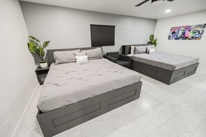 A modern bedroom with two beds, a ceiling fan, a black window blind, and a large abstract painting on the wall. - ZZ KC* (2520 Castlesands) % Elvis House 4BD/3BA Sleeps 12 (Las Vegas)