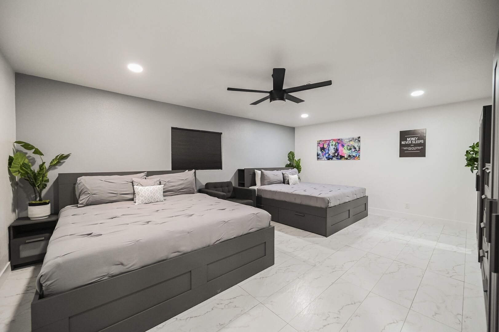 A modern bedroom with two beds, a ceiling fan, and a poster on the wall.