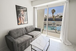 A modern living room with a grey sofa, a marble coffee table, and a large window with a view of a pool and palm trees. - ZZ KC* (2520 Castlesands) % Elvis House 4BD/3BA Sleeps 12 (Las Vegas)