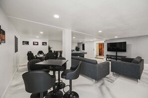 A modern living room with a sofa, a TV, and a dining area with chairs and a table. - ZZ KC* (2520 Castlesands) % Elvis House 4BD/3BA Sleeps 12 (Las Vegas)