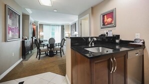 A modern kitchen with a black countertop, stainless steel sink, and wooden cabinets. There is a dining area with a table and chairs visible in the background. - SVS: One Bedroom | Strip View Balcony | MGM Signature (Las Vegas)