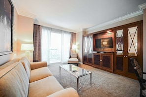 Ein Hotelzimmer mit einer Couch, einem Couchtisch, einem Fernseher und einem großen Fenster mit Vorhängen.