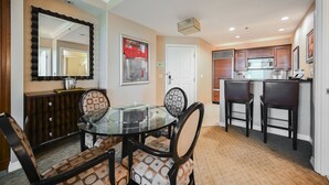 A dining area with a glass table and patterned chairs, a kitchen with wooden cabinets, and a framed artwork on the wall. - 1BD/2BA • Balcony • No Resort Fee • Free Parking E26A3 (Las Vegas)