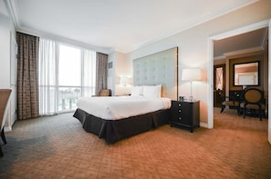 Ein Hotelzimmer mit einem großen Bett, einem Nachttisch, einem Sessel und Blick ins Freie durch ein großes Fenster.