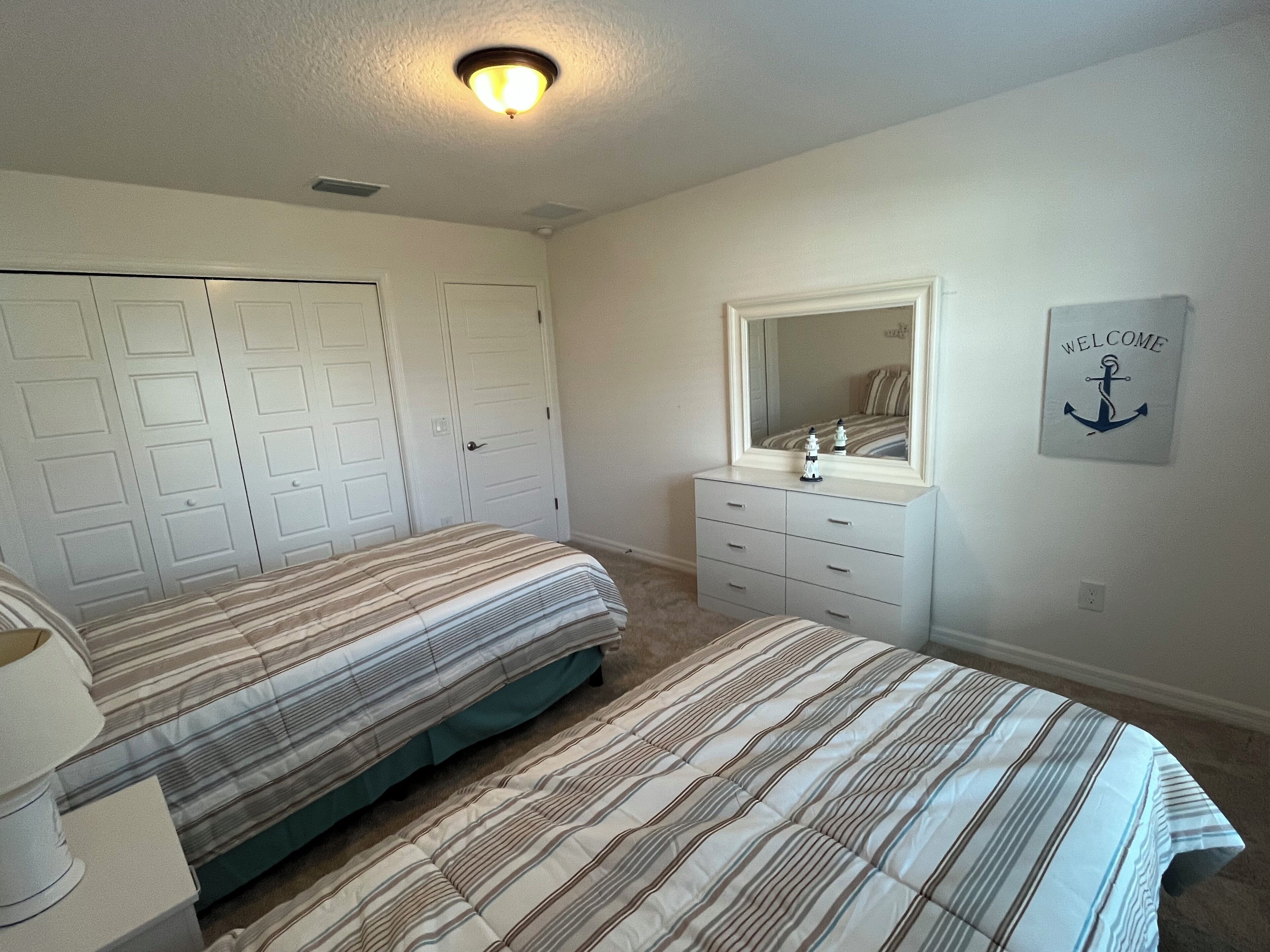 Une chambre avec deux lits, une commode, un miroir et une pancarte de bienvenue.