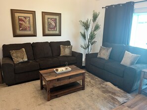 Ein Wohnzimmer mit zwei dunklen Sofas, einem Holztisch und einer Topfpflanze.