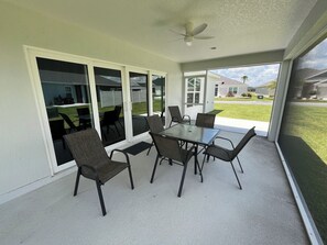 Un patio couvert avec une table et des chaises en verre, un ventilateur de plafond et une vue sur un quartier résidentiel.