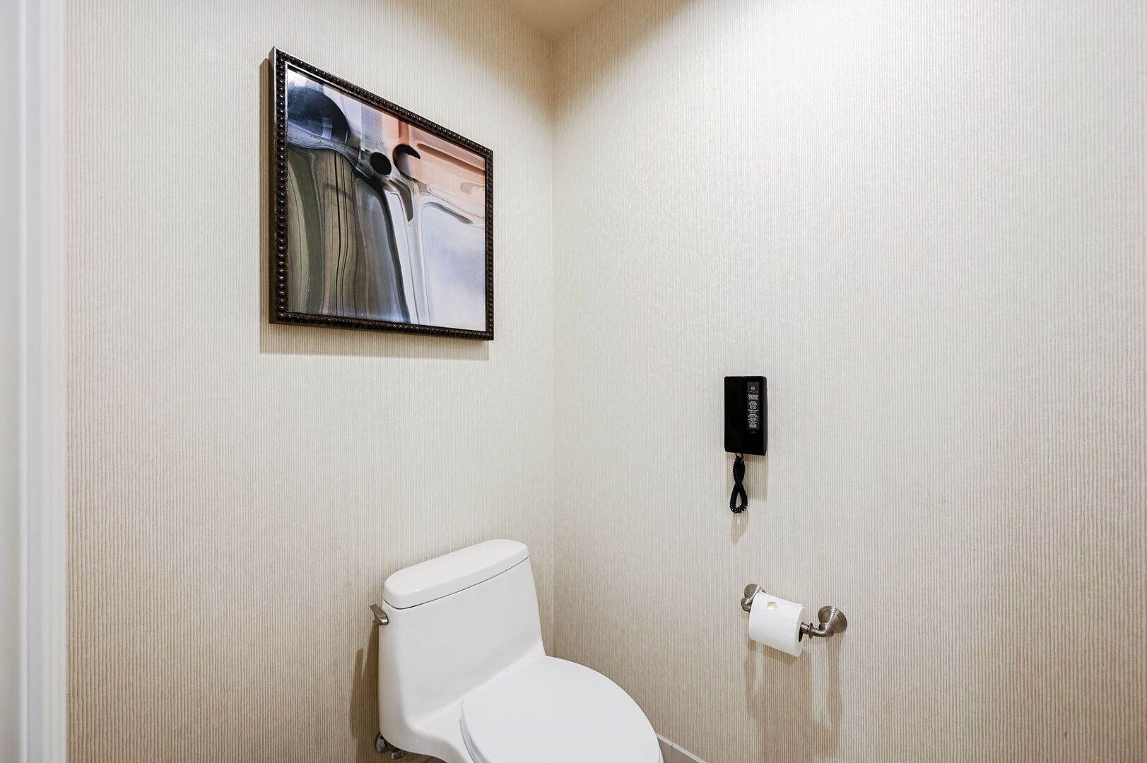 A bathroom with a toilet, a hand dryer, and a wall-mounted phone.
