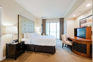A hotel room with a bed, a desk with a television, a chair, and a nightstand with a lamp. - SPHERE Strip View One Bedroom | Balcony| Signature at MGM F38Q3 (Las Vegas)