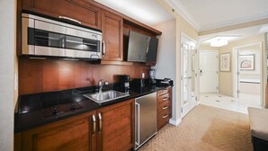 A kitchen with wooden cabinets, a stainless steel refrigerator, a microwave, a coffee maker, and a flat-screen TV. - SVS: Strip View Studio | Signature at MGM (Las Vegas)