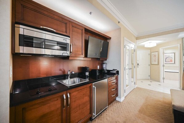 A kitchen with wooden cabinets, a stainless steel refrigerator, a microwave, a coffee maker, and a flat-screen TV. - Strip View Studio • No Resort Fee • Free Parking B2O1 (Las Vegas)