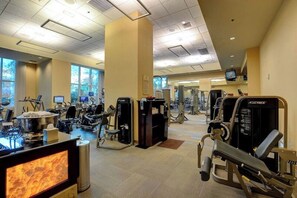 Ein Fitnessstudio mit verschiedenen Trainingsgeräten, einem Fernsehbildschirm und großen Fenstern.