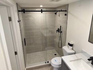 Une salle de bain moderne dotĂ©e dâune douche Ă parois de verre, de toilettes et dâun lavabo avec un plan de travail en marbre.