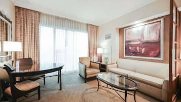 A hotel room with a dining table, two chairs, a sofa, a coffee table, a lamp, and a painting on the wall.