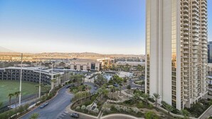 Un edificio moderno di grandi dimensioni, immerso in un'area verde con palme e una strada.